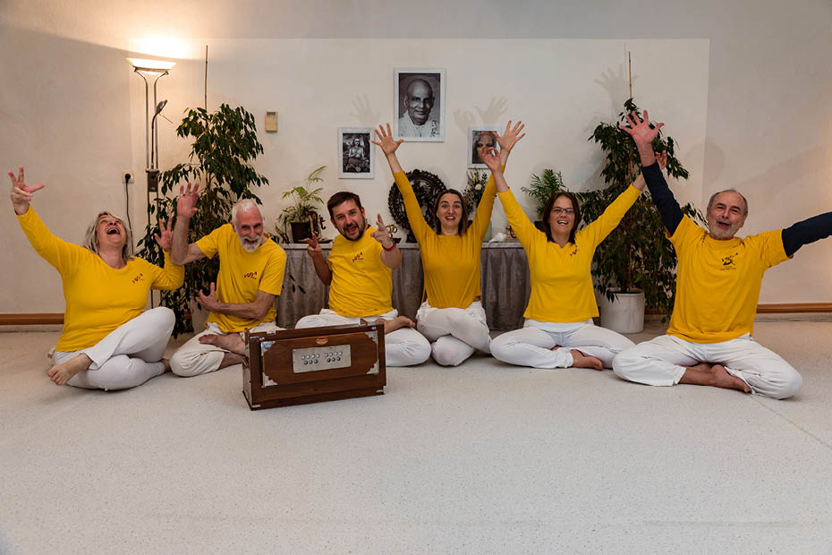 Gruppenbild: sechs Personen sitzen nebeneinander auf dem Boden in Yogaposen und jubeln | Über uns | Yoga Vidya Bayreuth